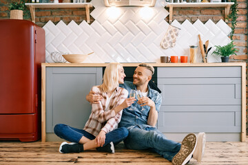 Romantic happy couple sitting on floor in kitchen and toasting champagne glasses © GVS