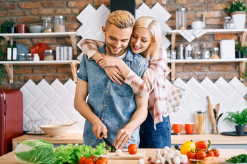 Smiling young couple cooking together vegetarian meal in the kitchen at home. Woman embracing man