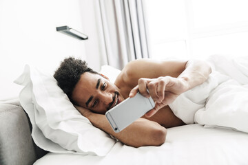 Photo of half-naked african american man using mobile phone and smiling