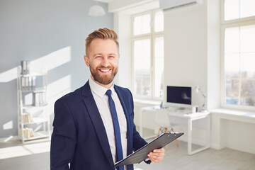 Positive businessman worker manager holds a clipboard in his hand smiling works in modern office.