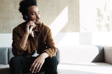 Photo of focused african american man using headphones and cellphone