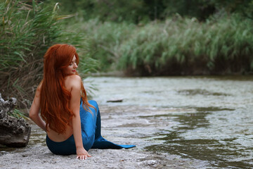 a mermaid in a blue suit with long red hair in the river  