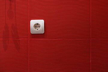 White socket installed in a red-tiled wall. Abstract bathroom background.
