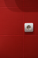 White socket installed in a red-tiled wall. Abstract bathroom background.