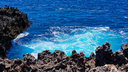 The turquoise blue sea is broken by volcanic rocks.