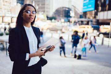 Confident black businesswoman waiting on street and surfing on smartphone