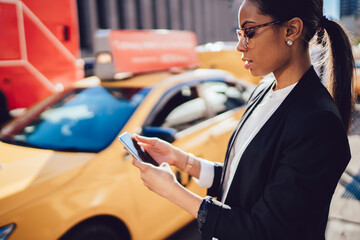 Confident corporate business woman using smartphone application for calling yellow taxi cab while...