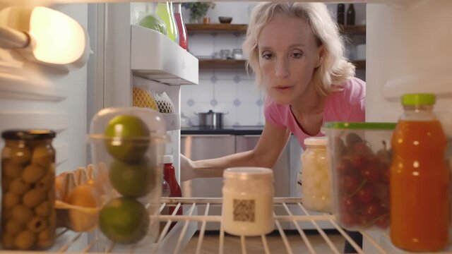 Mature woman taking yogurt from refrigerator in kitchen