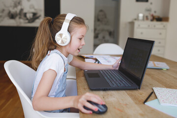 beautiful young girl with headphones and laptop is doing homeschooling during corona covid 19