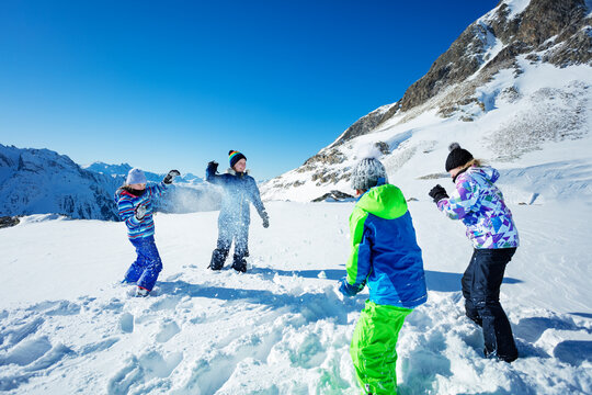 Group of four children play snowball fight winter game in the mountains throwing snow and wearing ski outfit