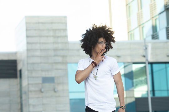 Young black man with curly hair smoking outdoors.