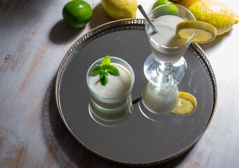 Glass and cup with refreshing lemon drink on tray and around lemons and limes