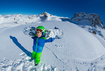 Wide mountain panorama and cute little smiling boy hold snowboard on shoulders view from above with mask off