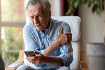 Senior man experiencing pain while using a smartphone at home
