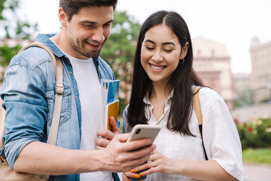 Image of joyful student couple talking and using cellphone while walking
