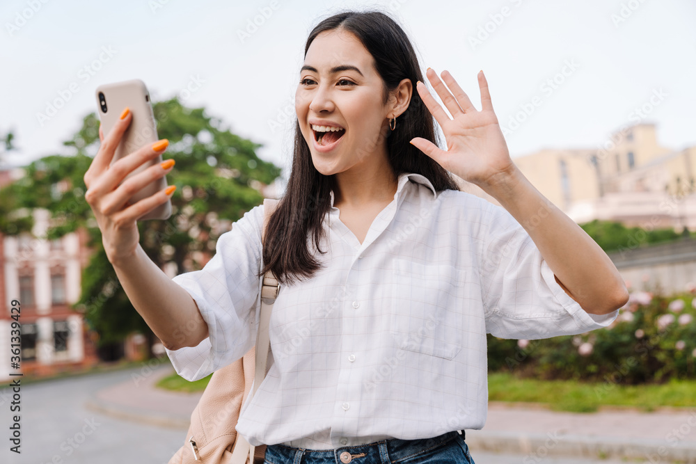 Wall mural Photo of happy asian woman using cellphone and waving hand