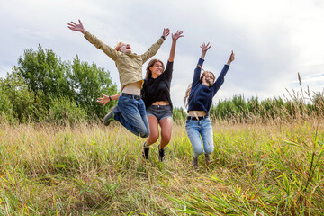 Summer holidays vacation happy people concept. Group of three friends boy and two girls jumping, dancing and having fun together outdoors. Picnic with friends on road trip in nature.