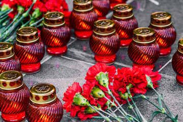 Red carnations on a marble slab and funeral lamps. Symbol of mourning, laying flowers at the memorial.