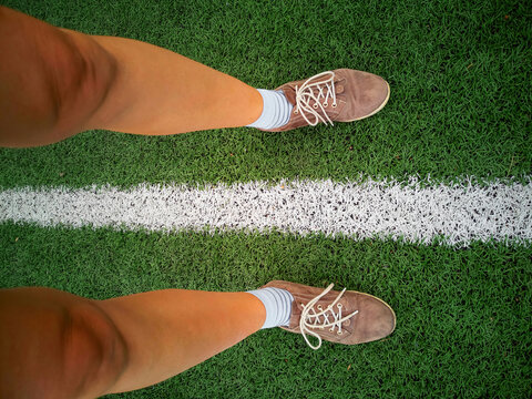 Two human legs on man-made green football field and white stripe between them