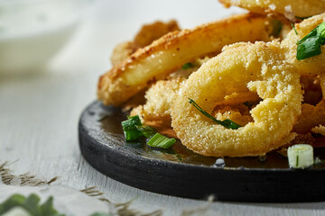 Onion rings in batter sprinkled with greens on a white background in a blur. Unhealthy but delicious food.