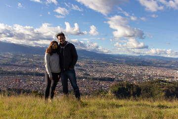  A couple standing and looking ahead on a hill, under a sky with sparse clouds and sunny, with a huge city in the background