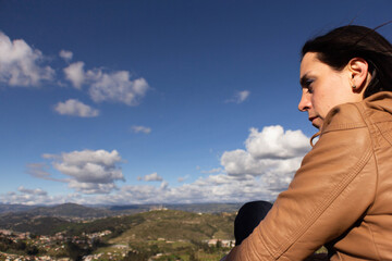 Naklejka premium sunny day with little cloudiness zero pollution, Girl looks at the horizon sitting on the grass to nature and a small town in the background