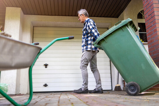 Senior man rolling garbage can
