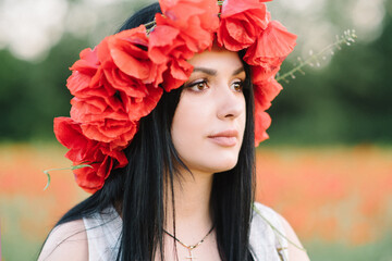 Portrait of a beautiful cute brunette girl in poppy field at sunset