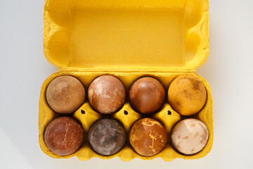 yellow box with eight original, unique colorful dragon or dinosaur looking like chicken Easter eggs, dyed with natural products (red wine, tea, coffee, carrots, turmeric, soy sauce)