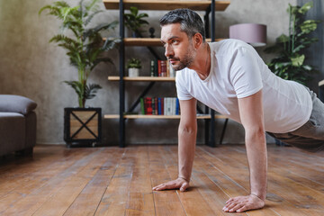 Concentrated middle adult man doing push ups exercise at home