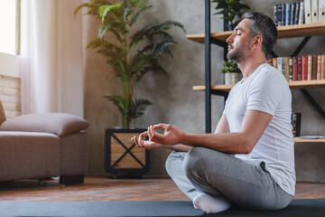 Meditation concept. Calm man meditating while sitting in lotus position relaxing doing yoga at home - obrazy, fototapety, plakaty