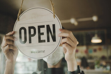 Open. barista, waitress woman wearing protection face mask turning open sign board on glass door in...