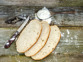 Slices of bread lie on a wooden table. Wheat flour is scattered, a knife for cutting bread.