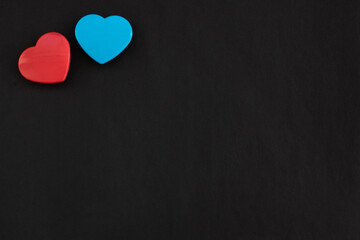 Two red and blue color hearts lying close together isolated at the top left corner of black paper background. Flat lay with empty space for text.