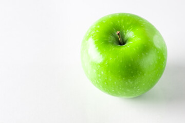 Green apple on a white background. An apple stands on a glass surface.
