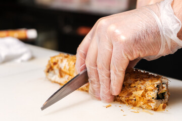 Sushi chef cuts a roll in tuna shavings with a knife on a white Board