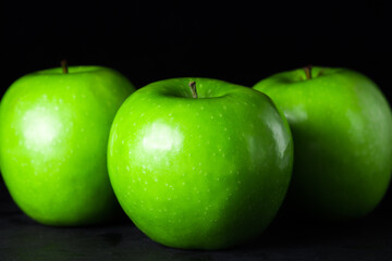 Green apples on a black background. Three apples stand next to each other. One apple in front