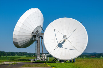 Zwei Parabolantennen einer Erdfunkstation zwischen grünen Feldern.