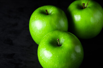 Green apples on a black background. Three apples stand next to each other. One apple in front