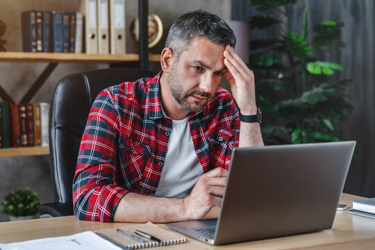 Middle aged man having stressful time working on laptop from home office