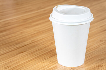 Mockup a disposable paper cup of coffee to go on wooden table.
