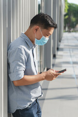 A businessman on the street with a blue face mask staring at his cell phone