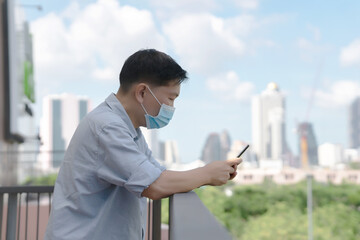 Businessman mask using mobile phone app texting outside of office in urban city with skyscrapers buildings in the background.