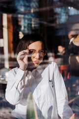 girl in glasses in reflection of a large showcase, a girl in a restaurant in a white shirt