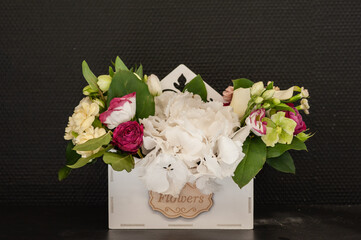 Flower arrangement with a white hydrangea in a white basket on a black background . Stylish flowers for sale. Selective focus.