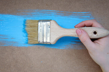 Paint brush surface with blue paint close up, hand with a brush to paint the walls.