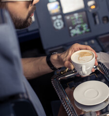 Coffee time during the flight. Young pilot in the aircraft in front of the dashboard with cup of tea. Private flight. The stewardess service the tea to captain in flight. Image with selective focus.