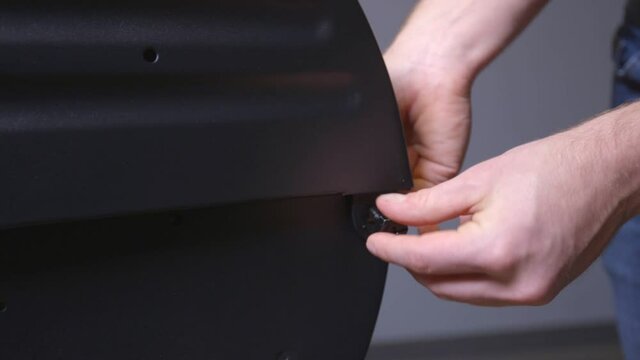 A close up shot of a mans two sturdy hands working on a DIY assembly grill, attaching the hood hinge to the body by inserting a heavy duty bolt and tightening it.