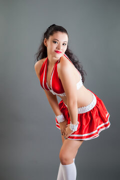 closeup young brunette woman in red cheerleader costume poses at camera in studio