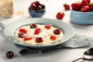 Oatmeal with milk and butter, with strawberries, and ripe cherries. A delicious and healthy breakfast, rich in vitamins and minerals.